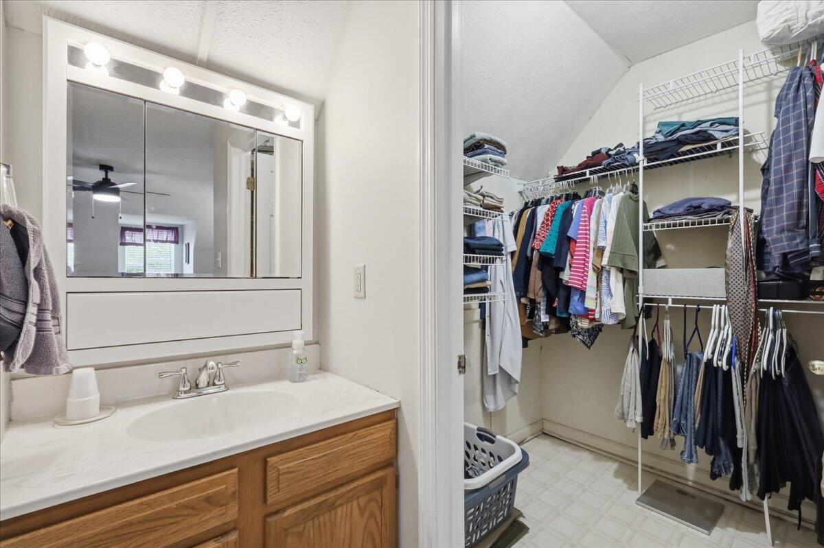 Bathroom vanity and illuminated mirror beside a spacious walk-in closet with wire shelving and hanging clothes.