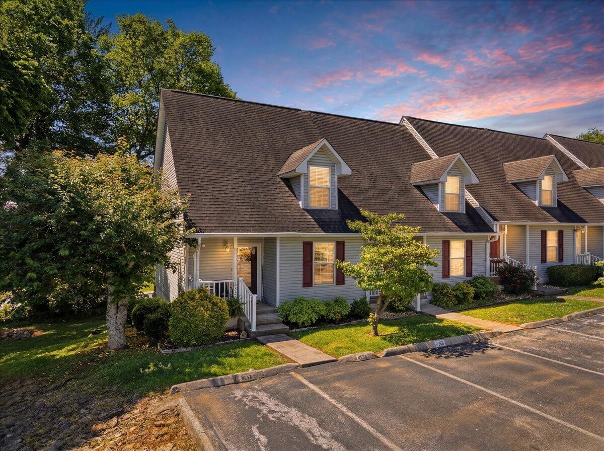 Attached gray homes with dormer windows and landscaped lawns beneath a pink evening sky.