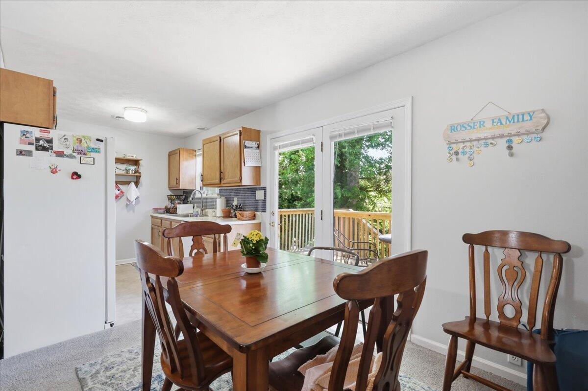Dining area with a wooden table beside a compact kitchen and glass doors opening to a leafy deck.