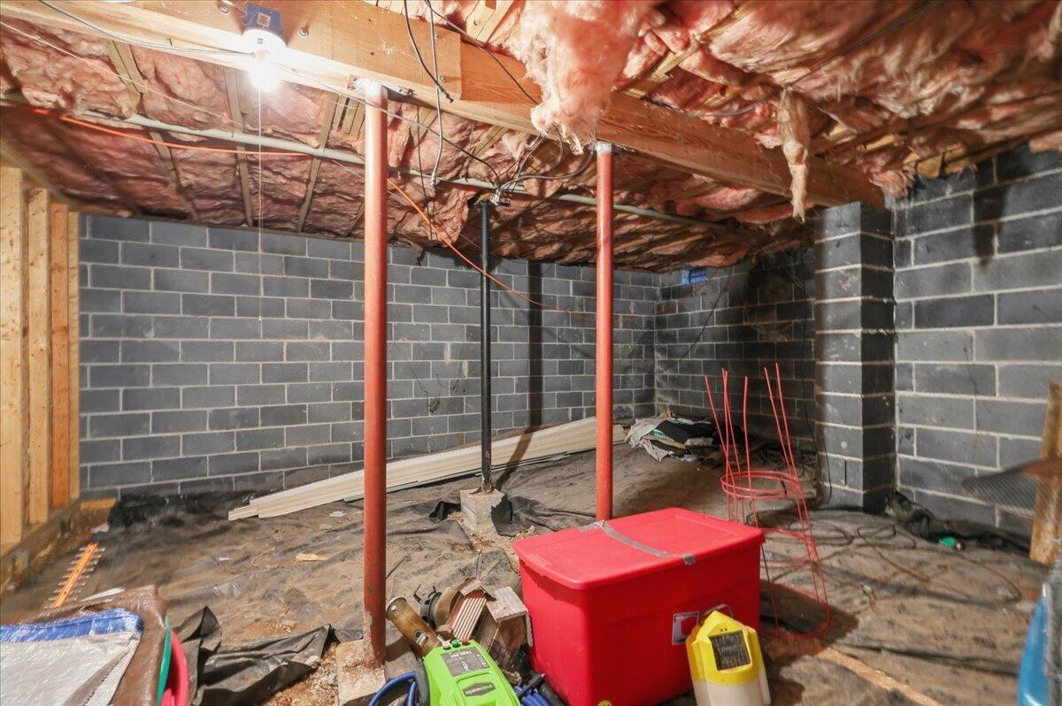 Unfinished basement with concrete block walls, exposed insulation, and red support posts.