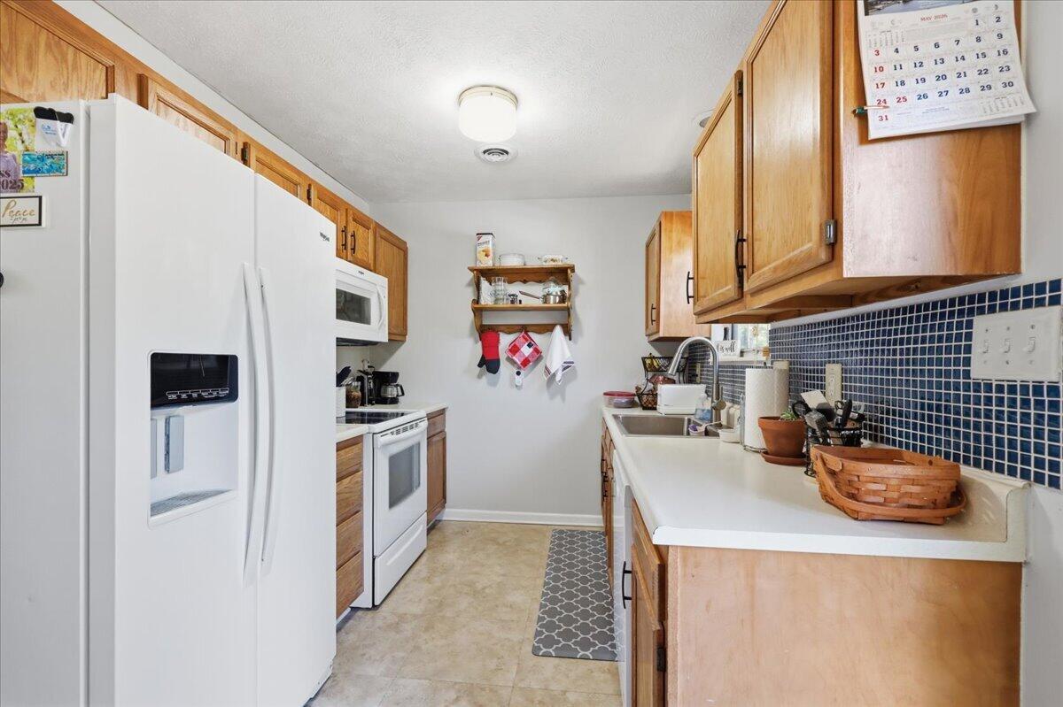 Galley kitchen with honey-colored cabinets, white appliances, and a blue tile backsplash.