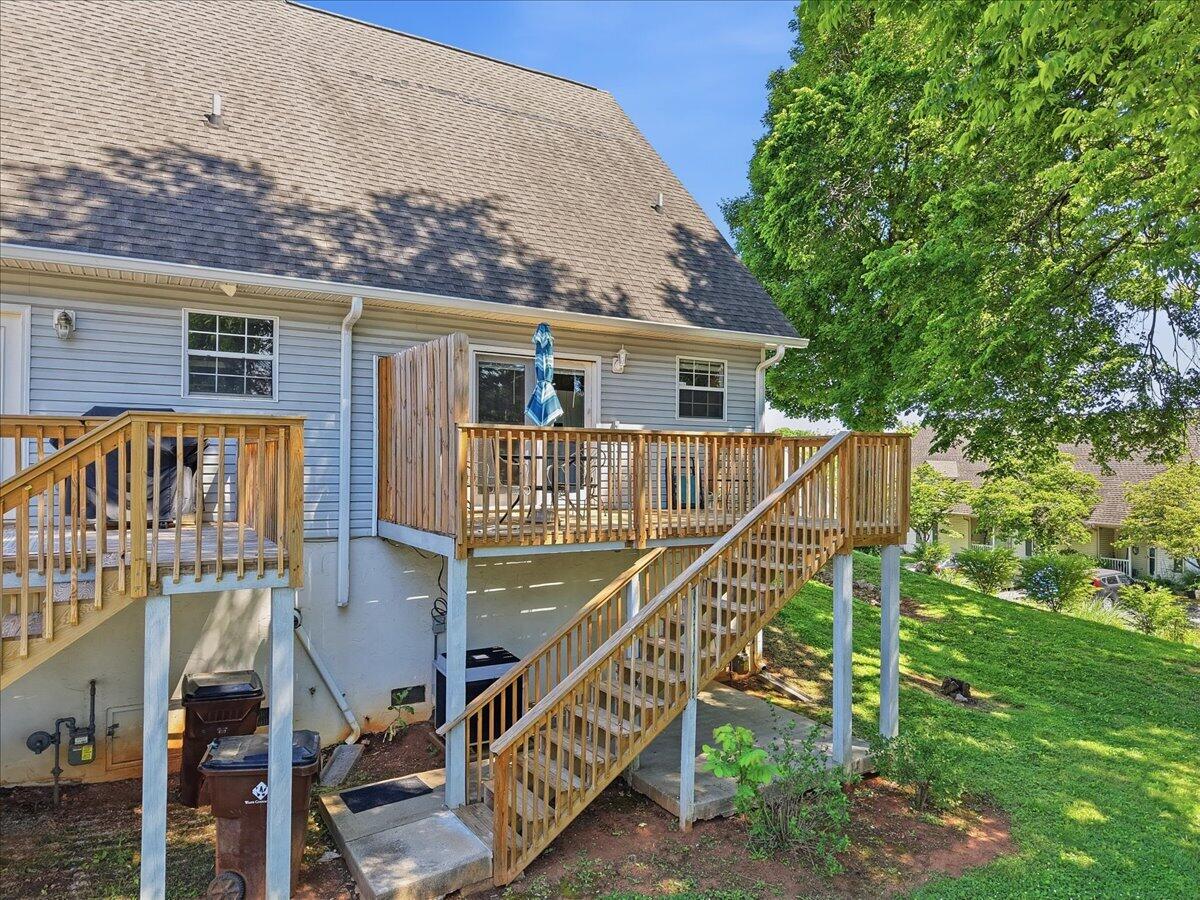 Rear of a blue-sided house with an elevated wooden deck and long stairs to the lawn.