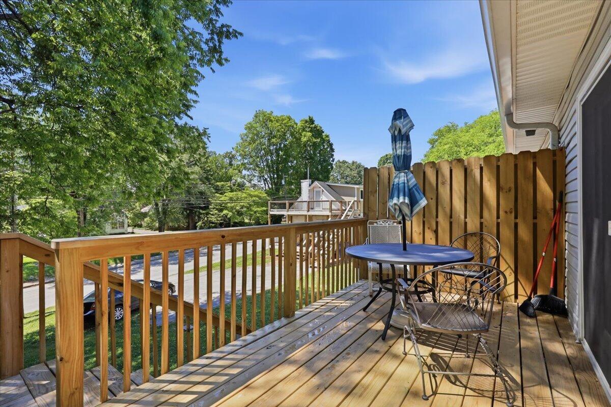 Wooden deck with dining set and closed umbrella beside a privacy fence and leafy trees.