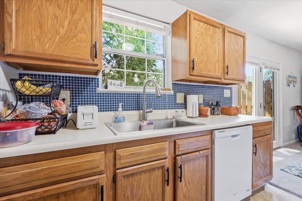 Kitchen with oak cabinets, blue tile backsplash, and a double sink beneath a large window.