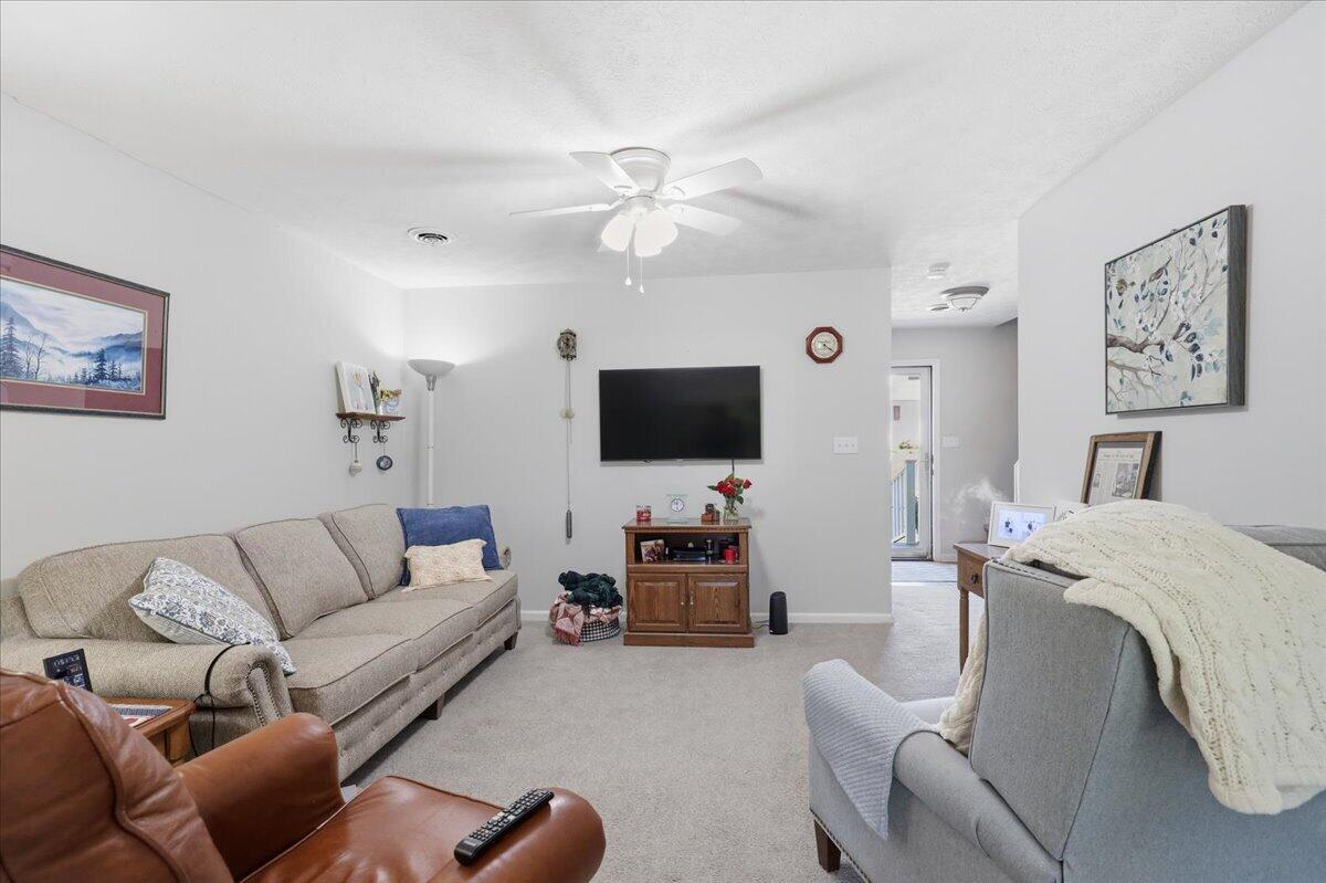 Living room with sofas, a leather recliner, wall-mounted television, and ceiling fan.