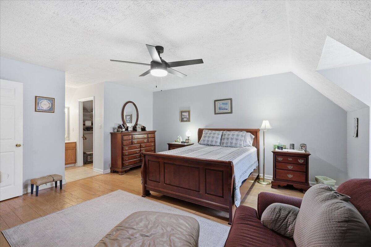 Furnished bedroom with a wooden bed, matching dressers, ceiling fan, and adjoining closet.