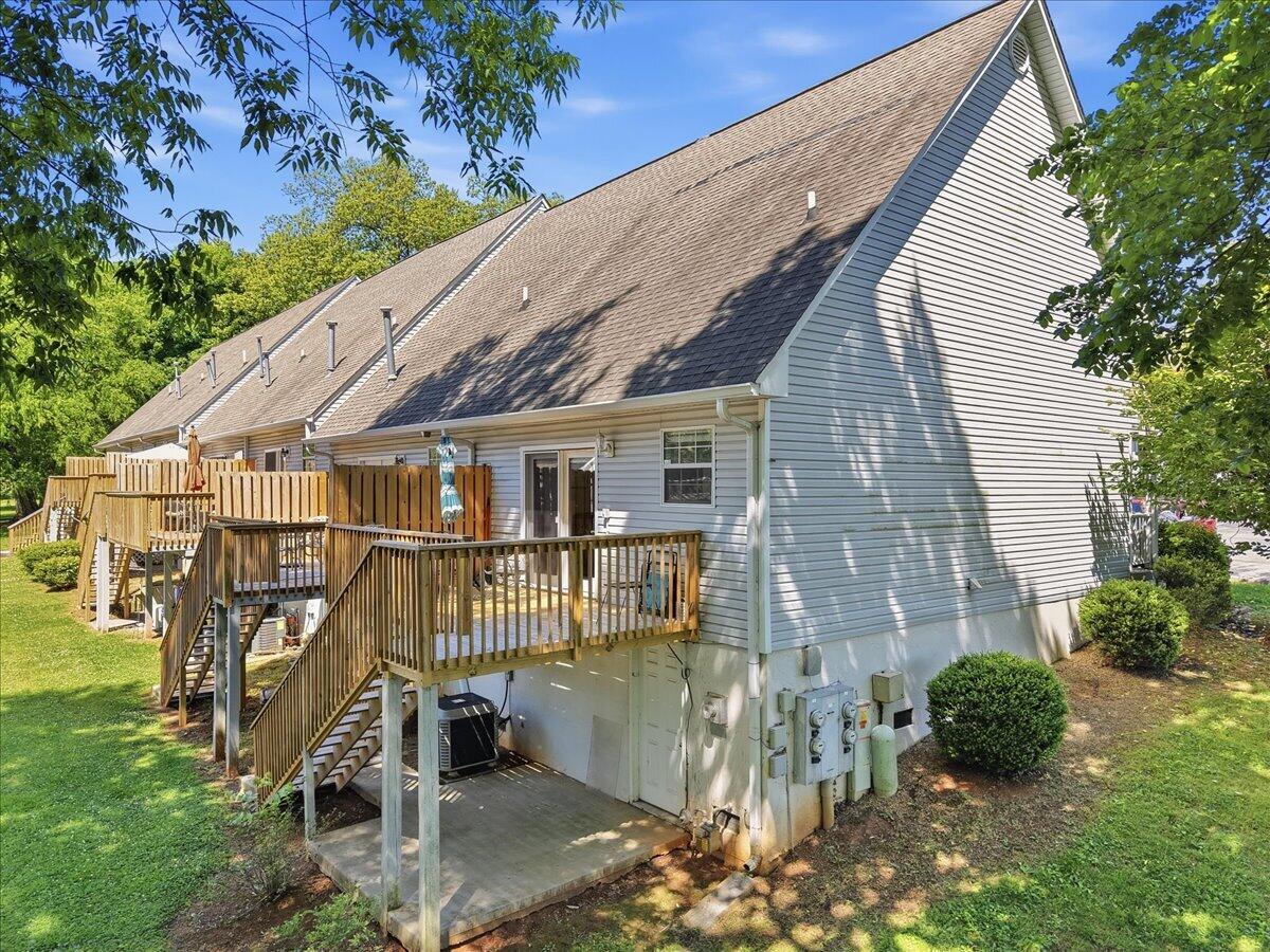 Rear exterior of a gray-sided home with raised wooden decks and stairs beside a shaded lawn.