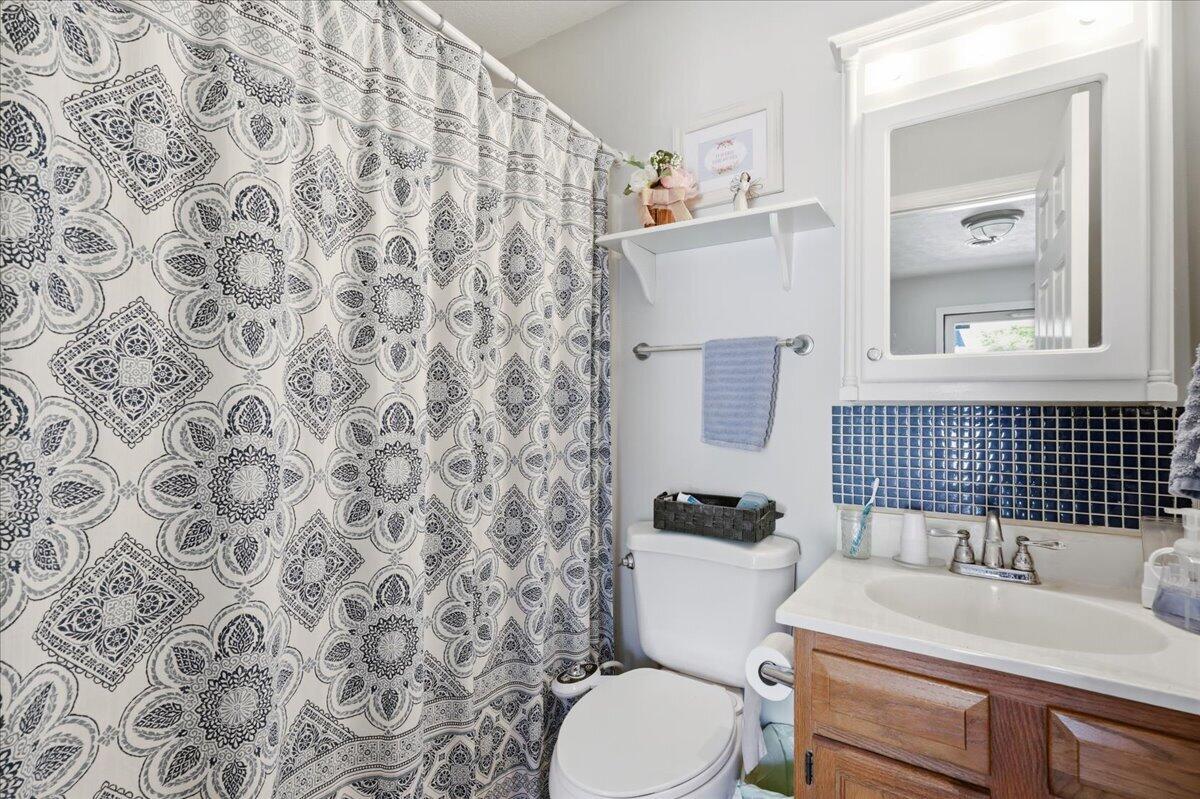 Bathroom with a patterned shower curtain, blue tile backsplash, and wood vanity.