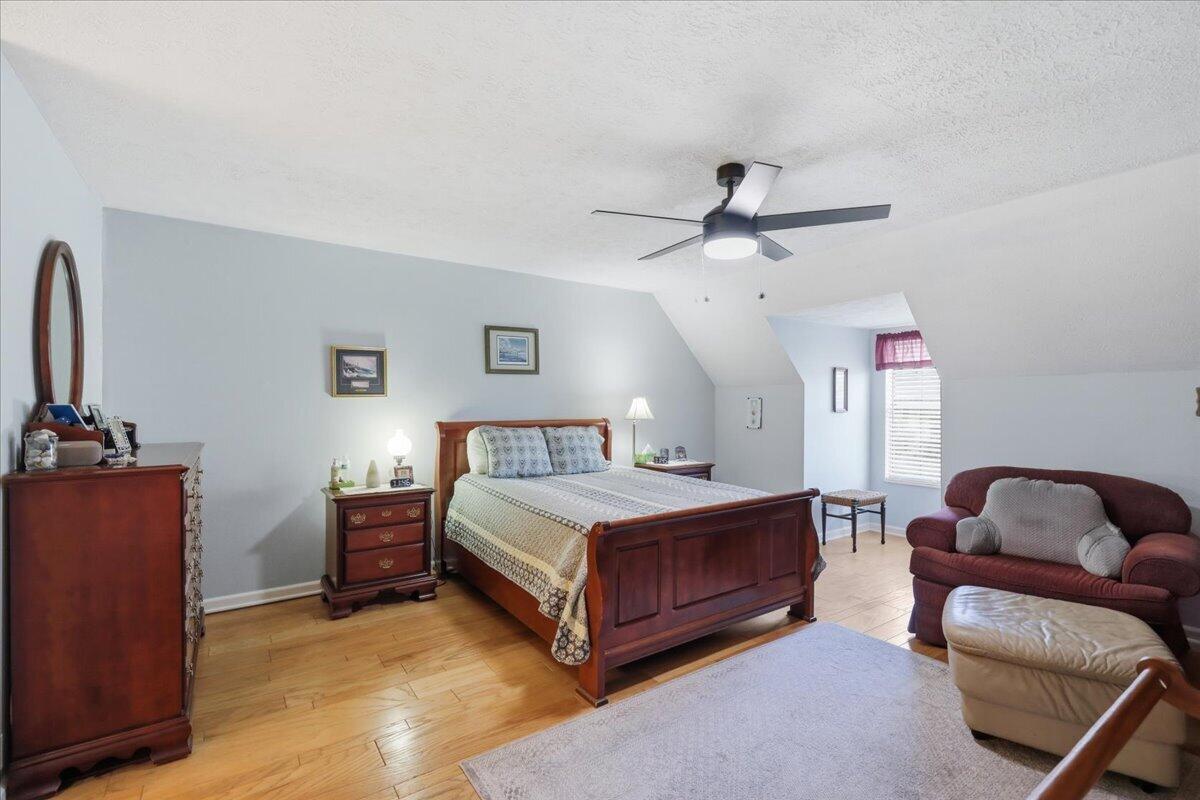 Furnished attic bedroom with a wooden bed, hardwood floors, ceiling fan, and sitting area.