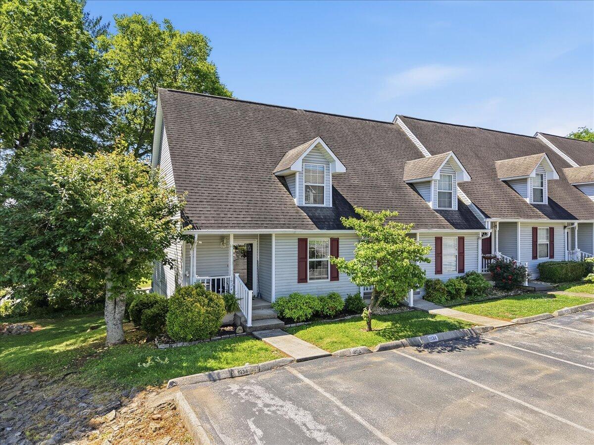 Townhouse exterior with dormer windows, red shutters, front porch, and parking spaces.