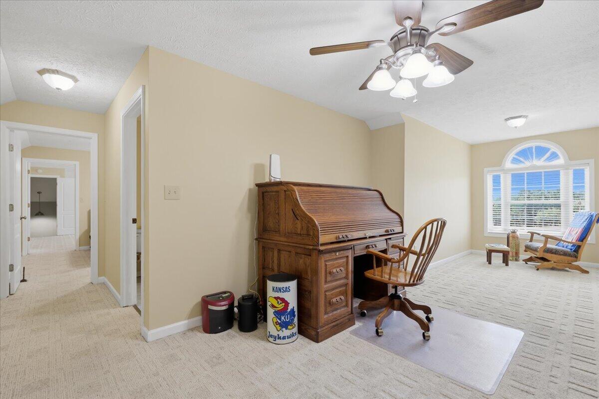 Home office with a wooden roll-top desk, rolling chair, and arched window with white shutters.