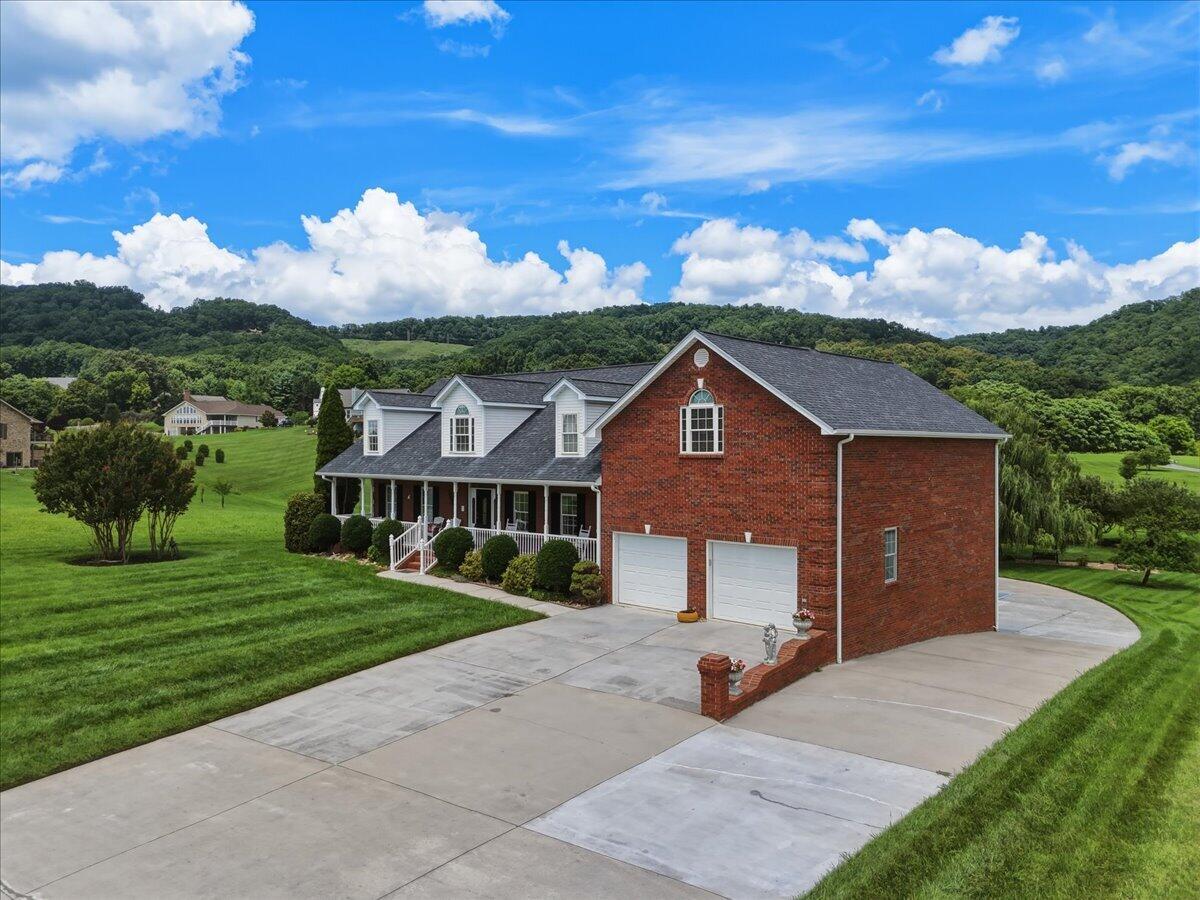 Red-brick home with white dormers, two garage doors, and a broad driveway on a green lawn.