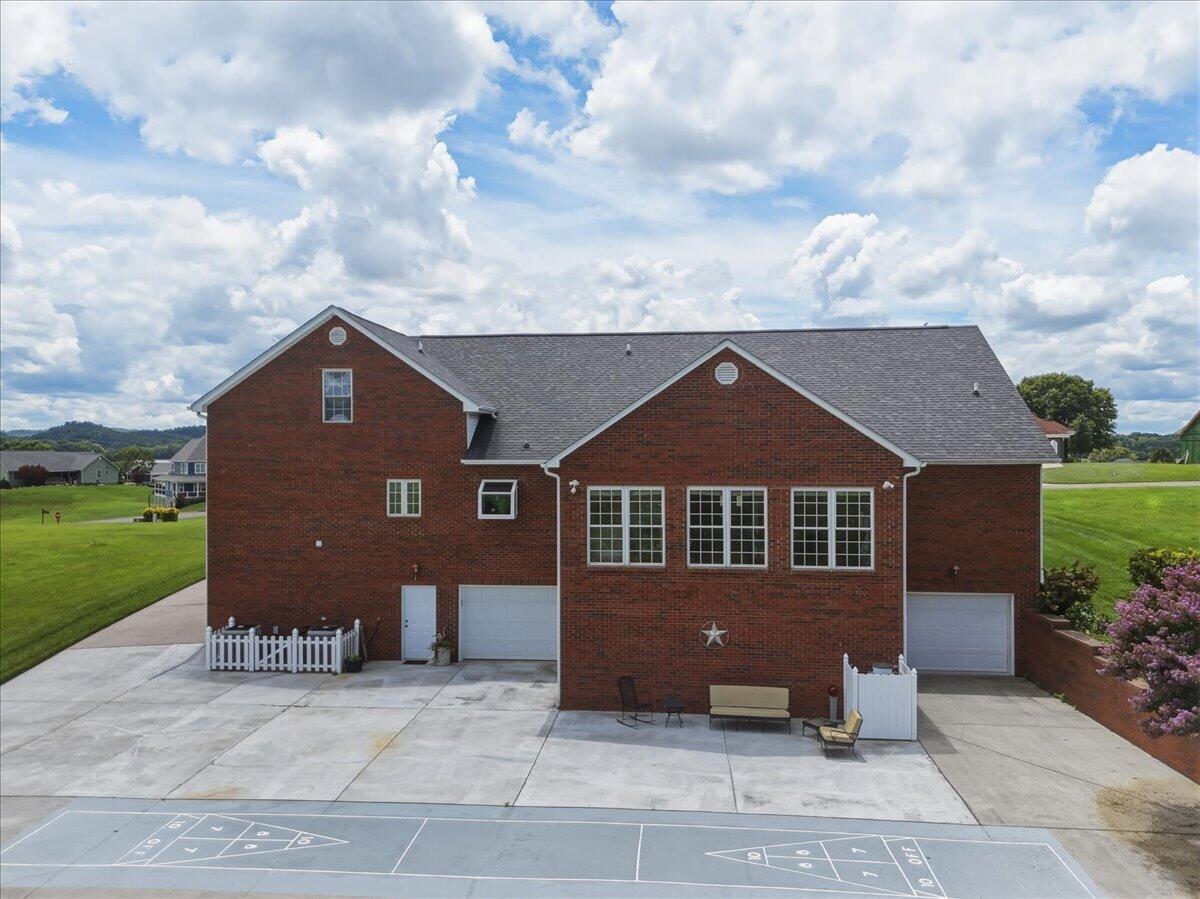 Red-brick home with multiple garage doors, a broad driveway, patio seating, and a shuffleboard court.