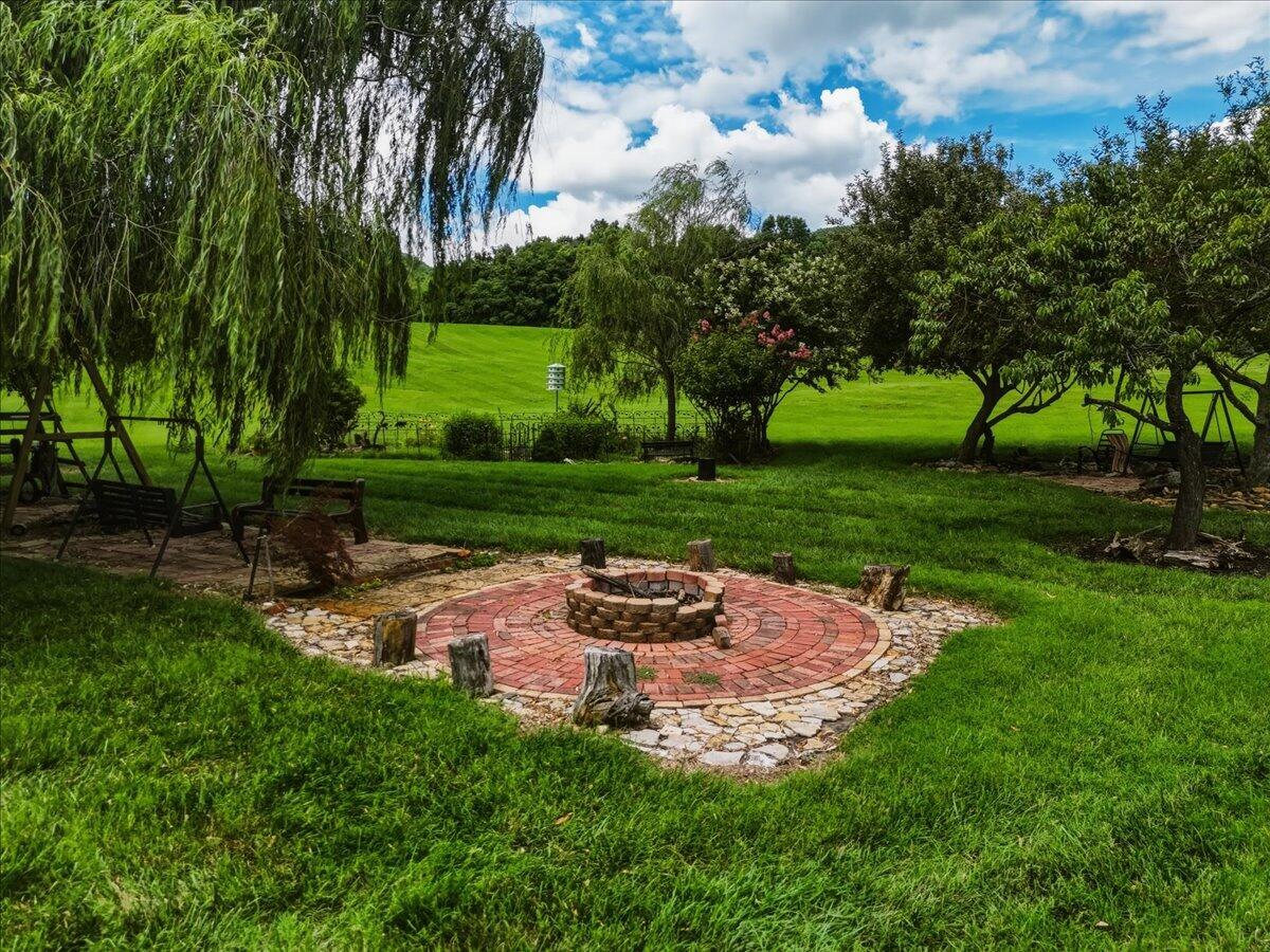 Backyard fire pit patio surrounded by lawn, mature trees, and outdoor swings.