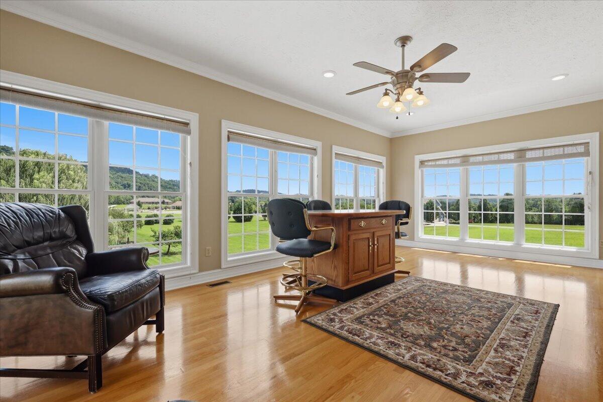 Sunroom with a wooden island, leather chairs, and large windows overlooking green grounds.