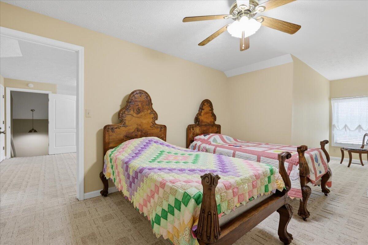 Bedroom with two carved wooden beds dressed in colorful patchwork quilts and a ceiling fan.
