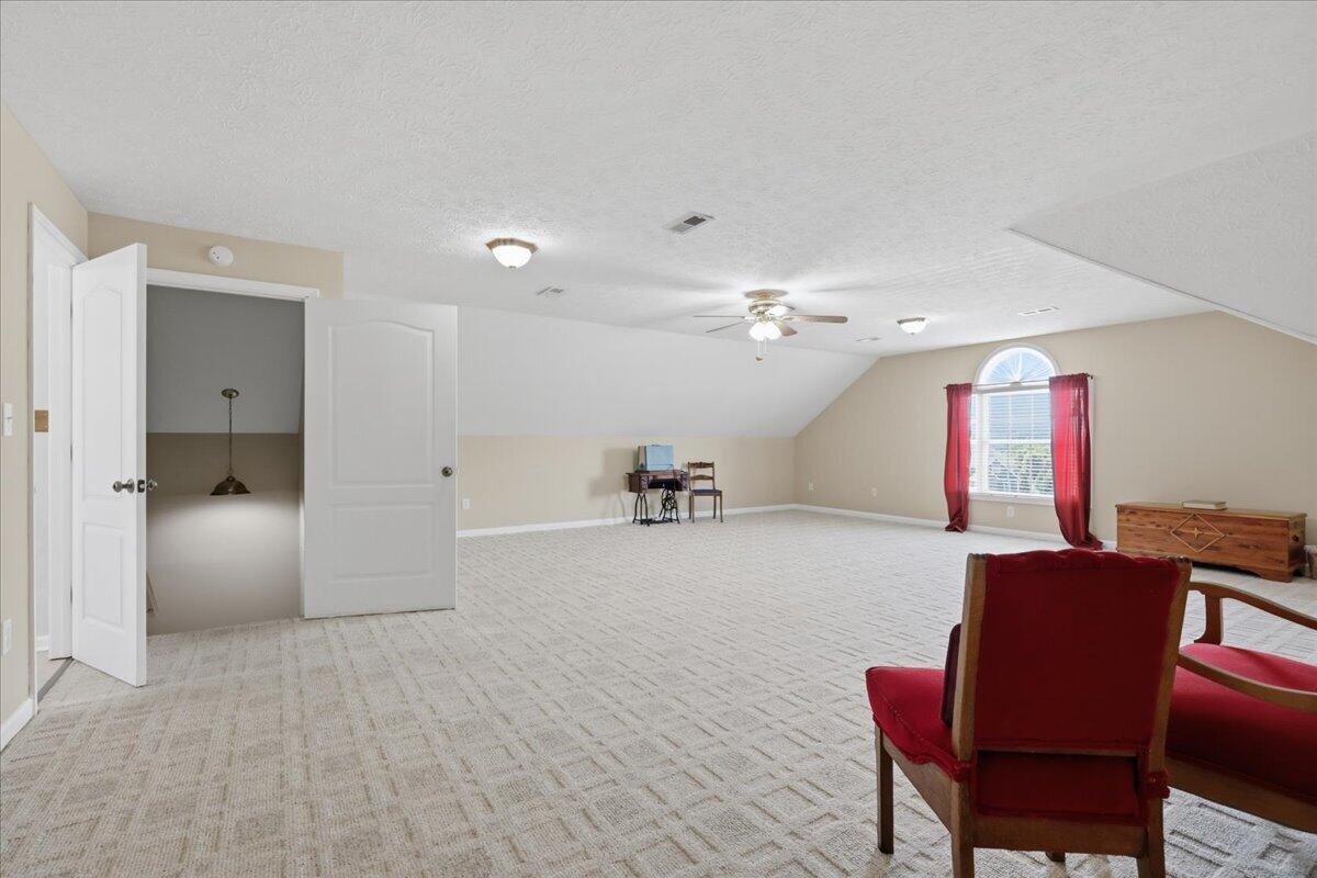 Furnished bonus room with a sloped ceiling, arched window, and red upholstered chairs.