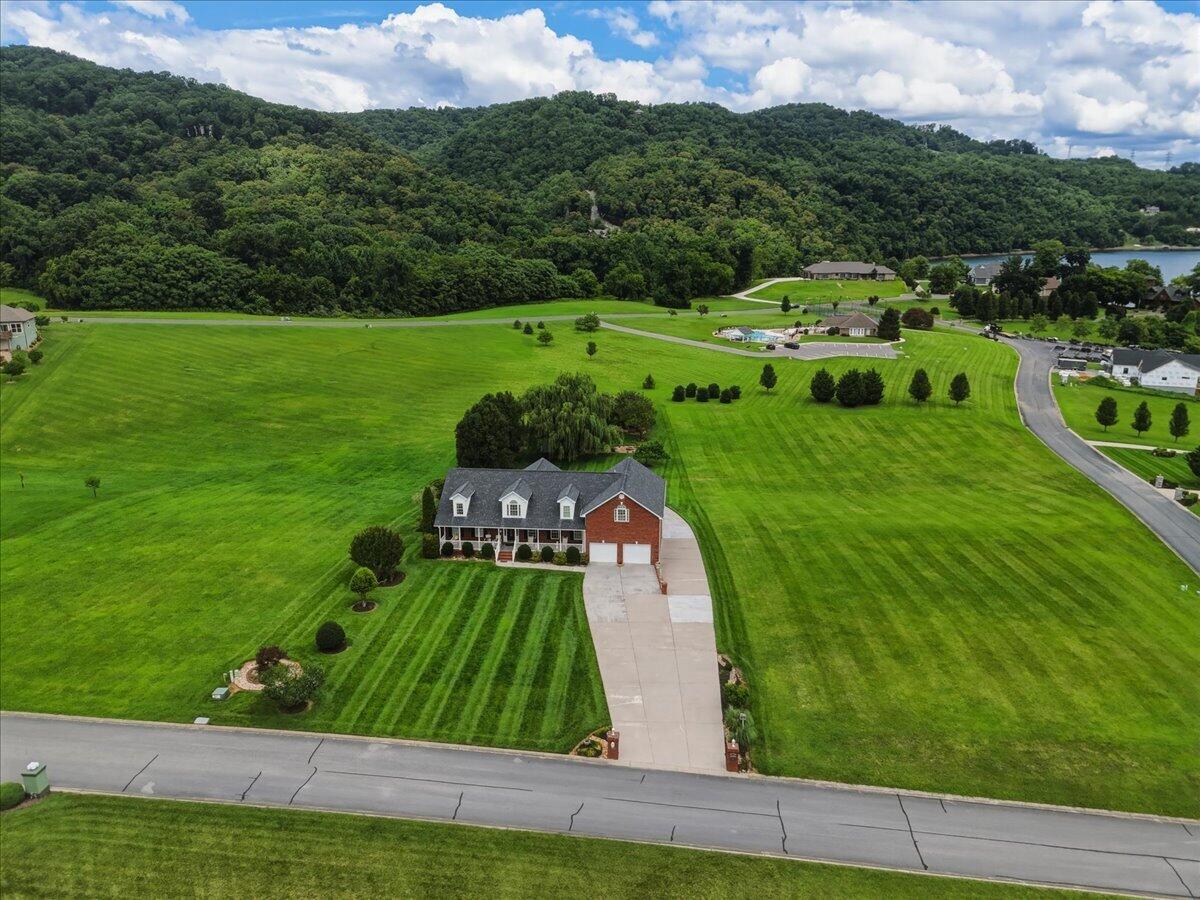 Aerial view of a brick-and-siding home with a long driveway and expansive striped lawn.