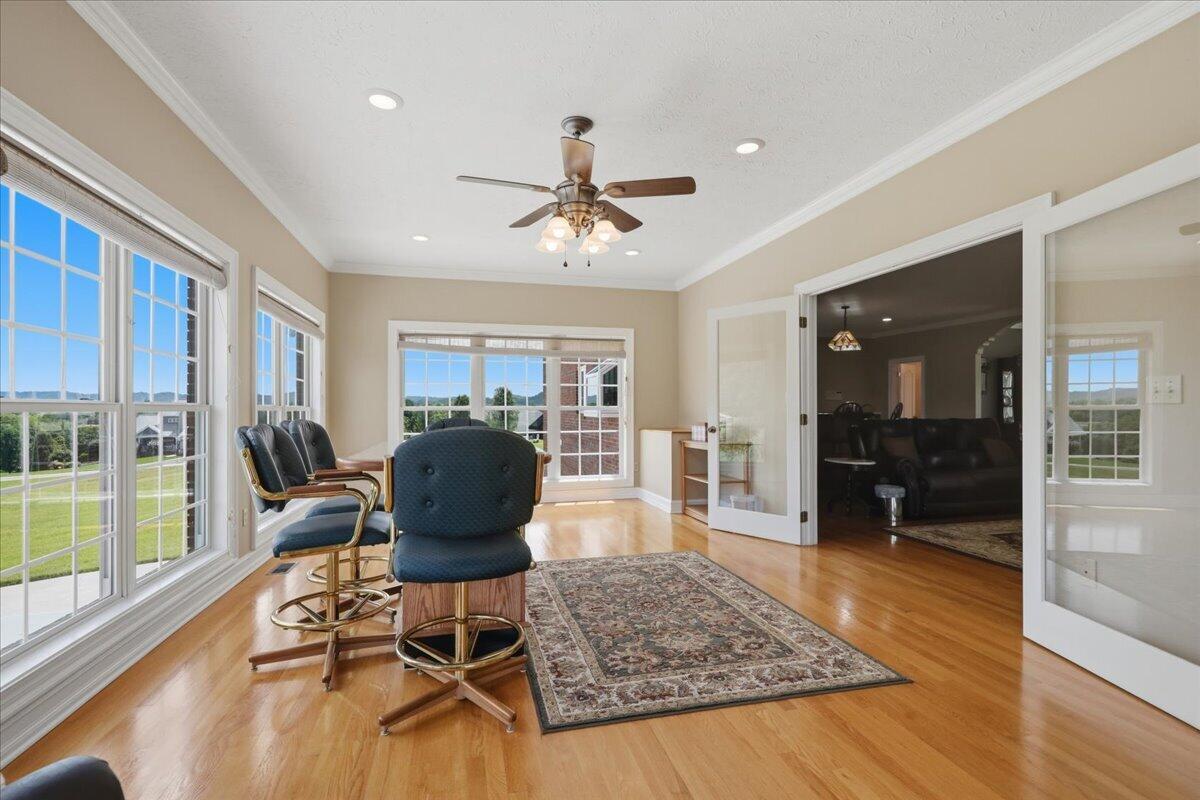 Sunroom with large windows, hardwood floors, upholstered chairs, and views of a green lawn and distant hills.
