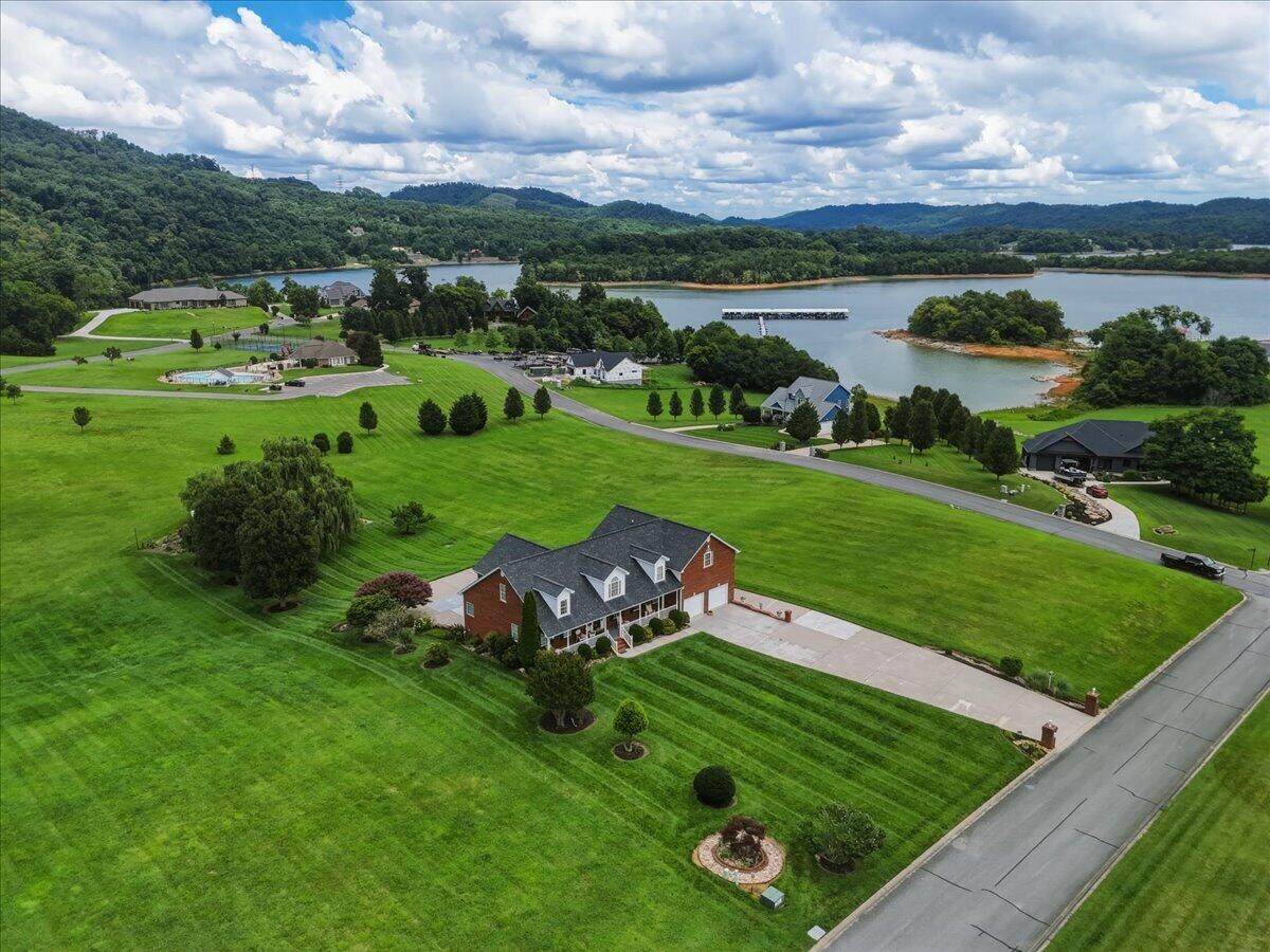 Aerial view of a brick home beside a broad lawn, with lake and hills beyond.