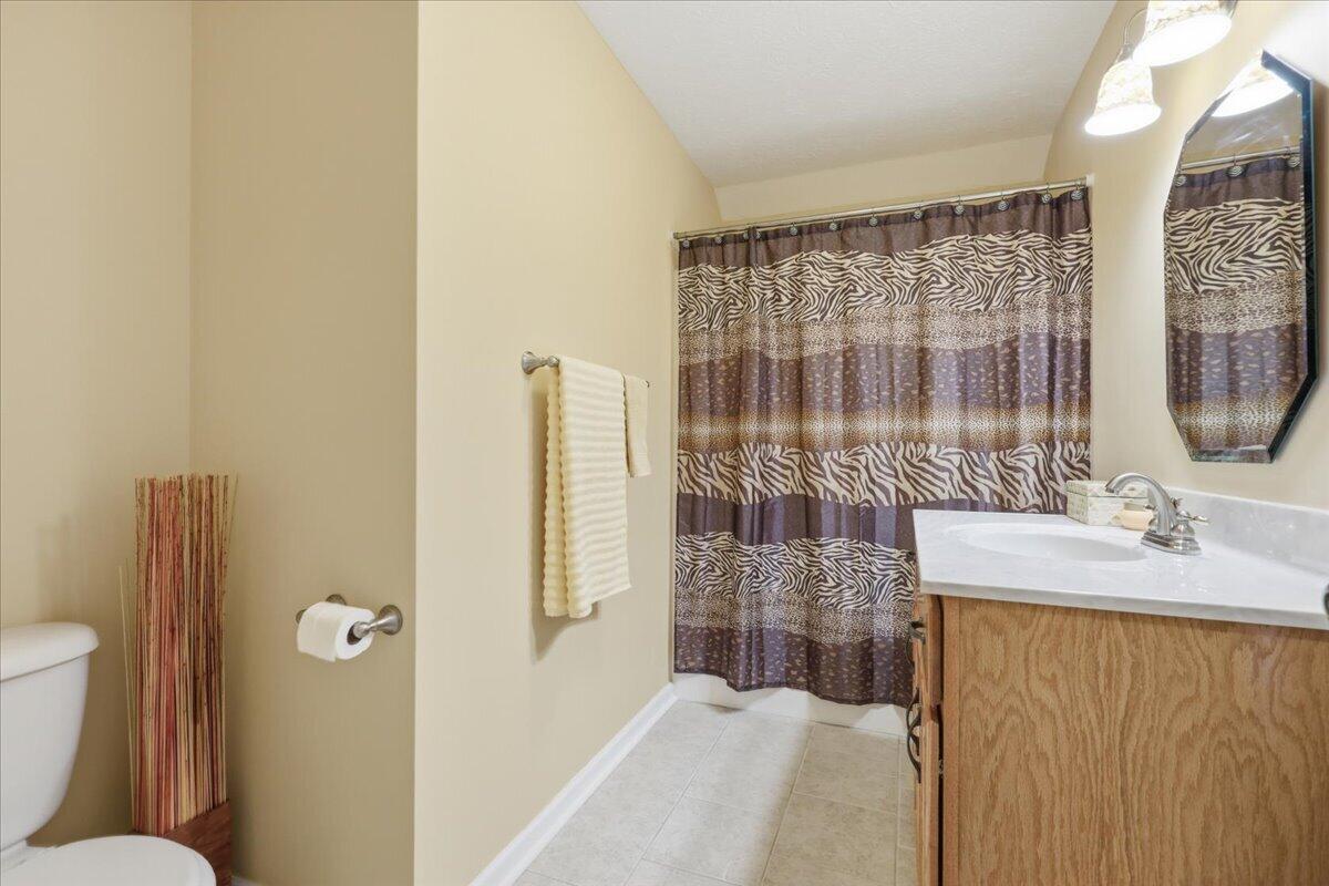 Bathroom with a wood vanity, oval mirror, and brown patterned shower curtain.