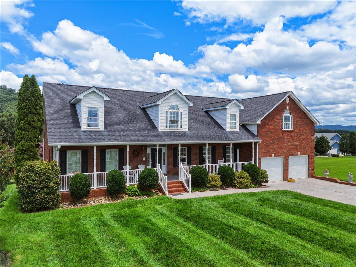 Red-brick house with white dormers, a covered porch, and a two-car garage behind a green lawn.
