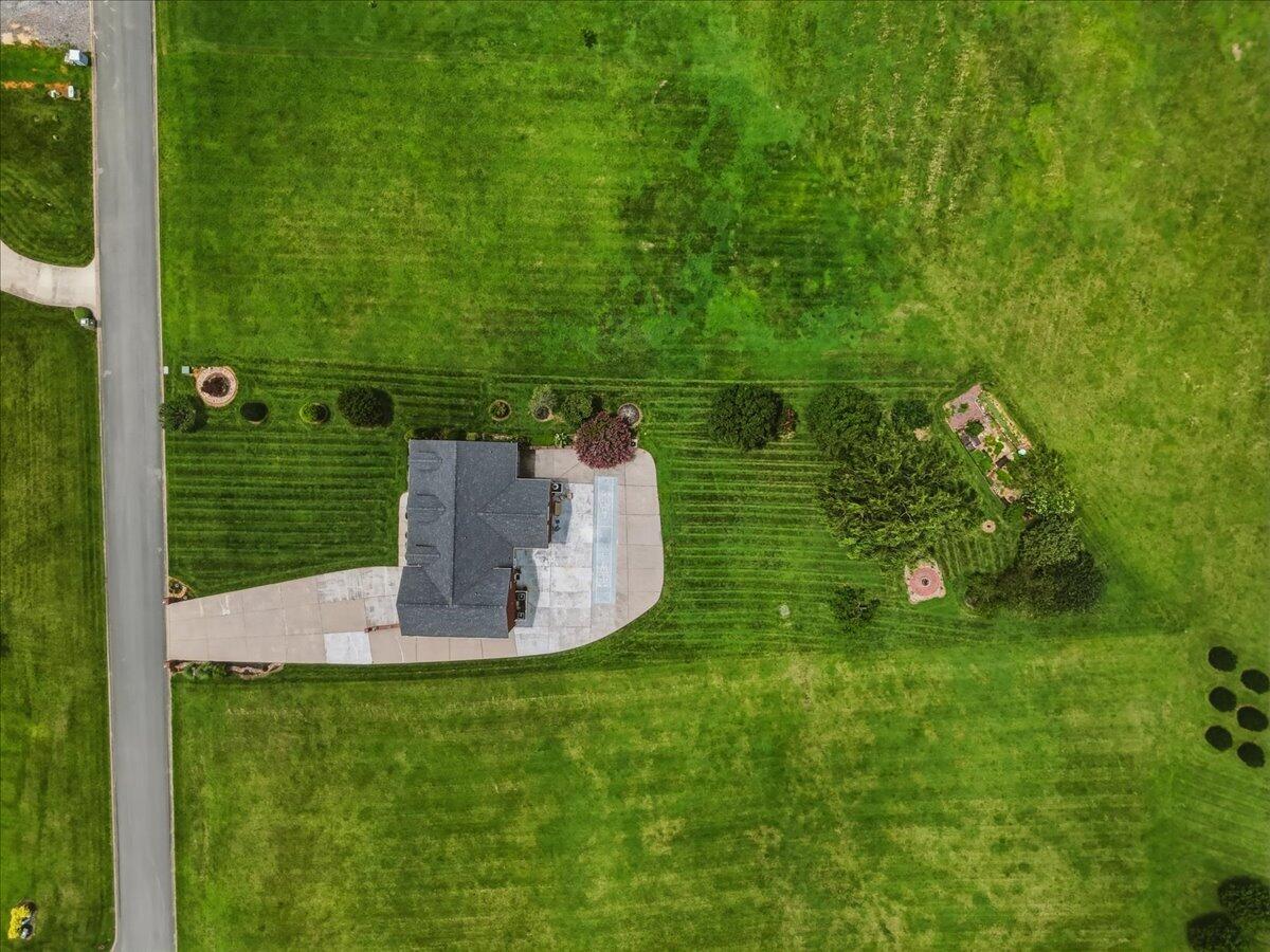 Aerial view of a house with a large lawn, paved driveway, patio, and narrow swimming pool.