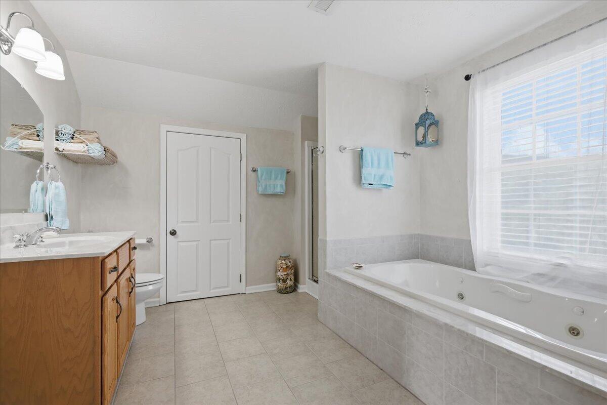 Bathroom with a jetted tub beneath a large window and a wood vanity.