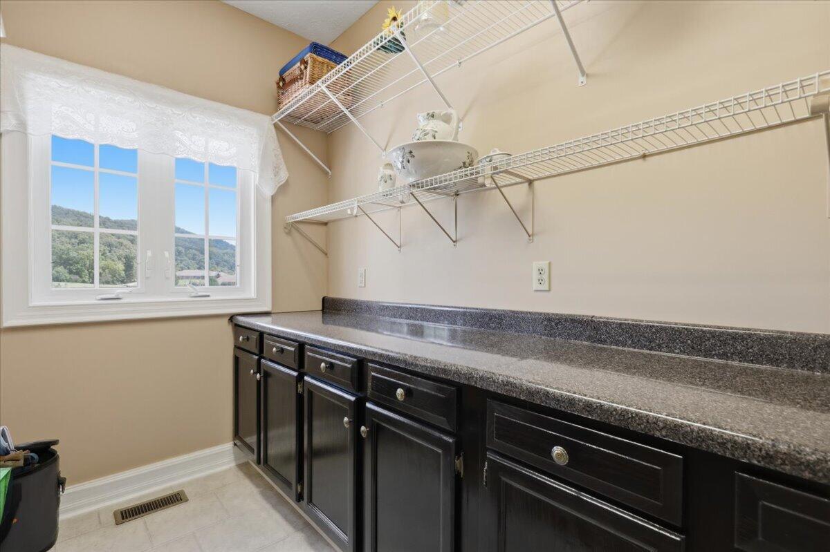 Pantry with dark cabinets, a long countertop, wire shelves, and a window overlooking wooded hills.