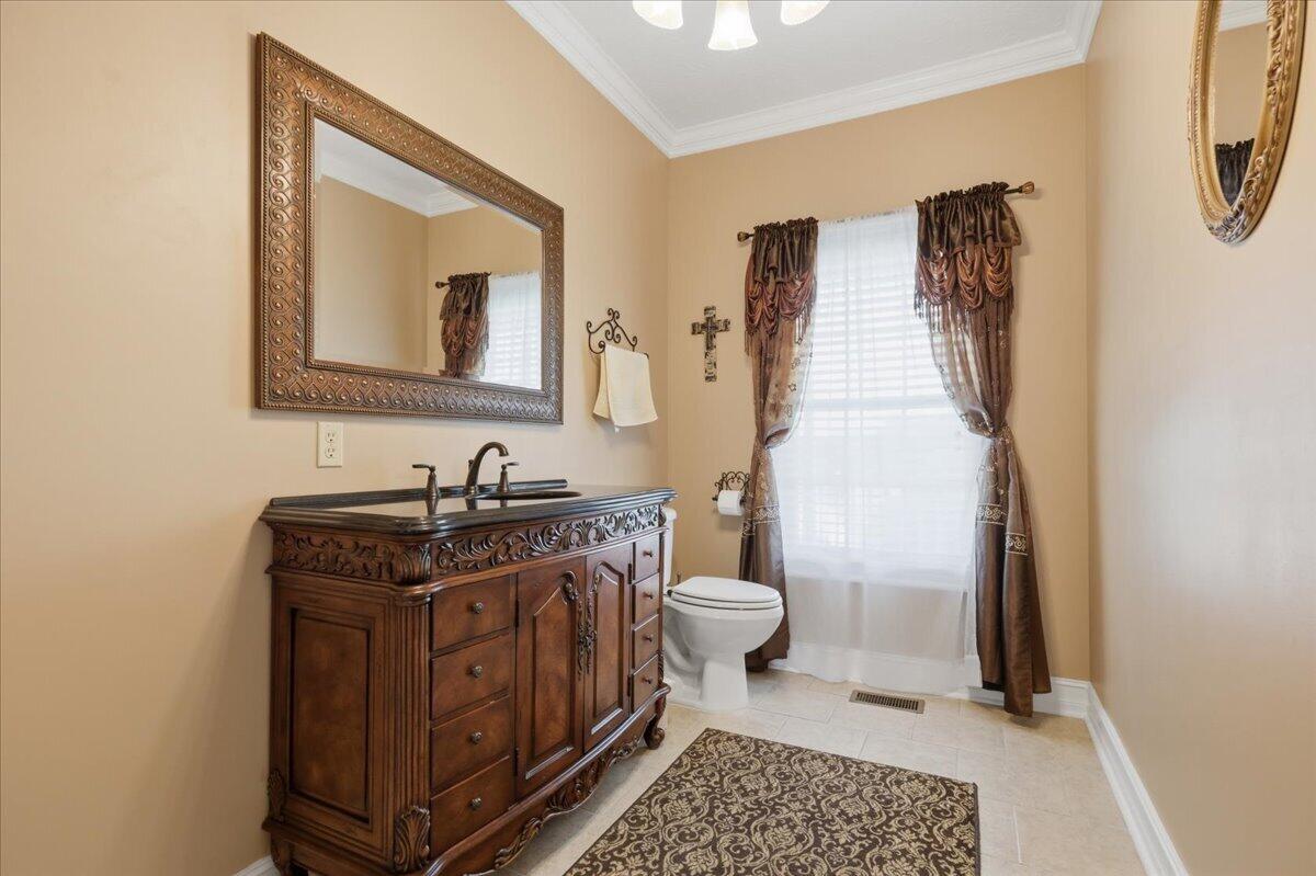 Bathroom with an ornate dark wood vanity, framed mirror, and curtained window.