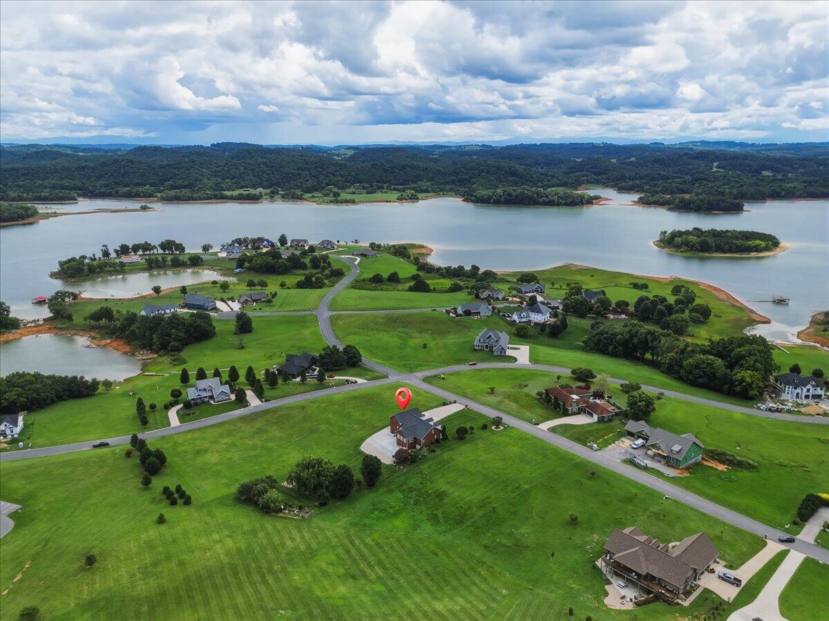 Aerial view of a lakeside neighborhood, with the featured home marked beside expansive green lawns.