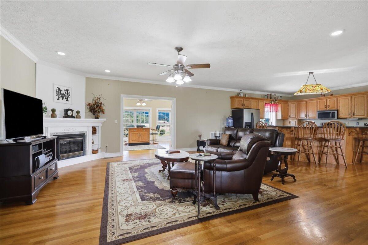 Living room with dark leather seating, patterned rug, white fireplace, and open kitchen.