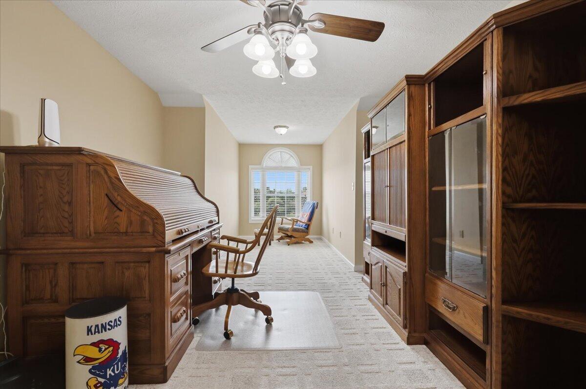 Home office with a roll-top desk, dark wood built-ins, and a window with blinds.