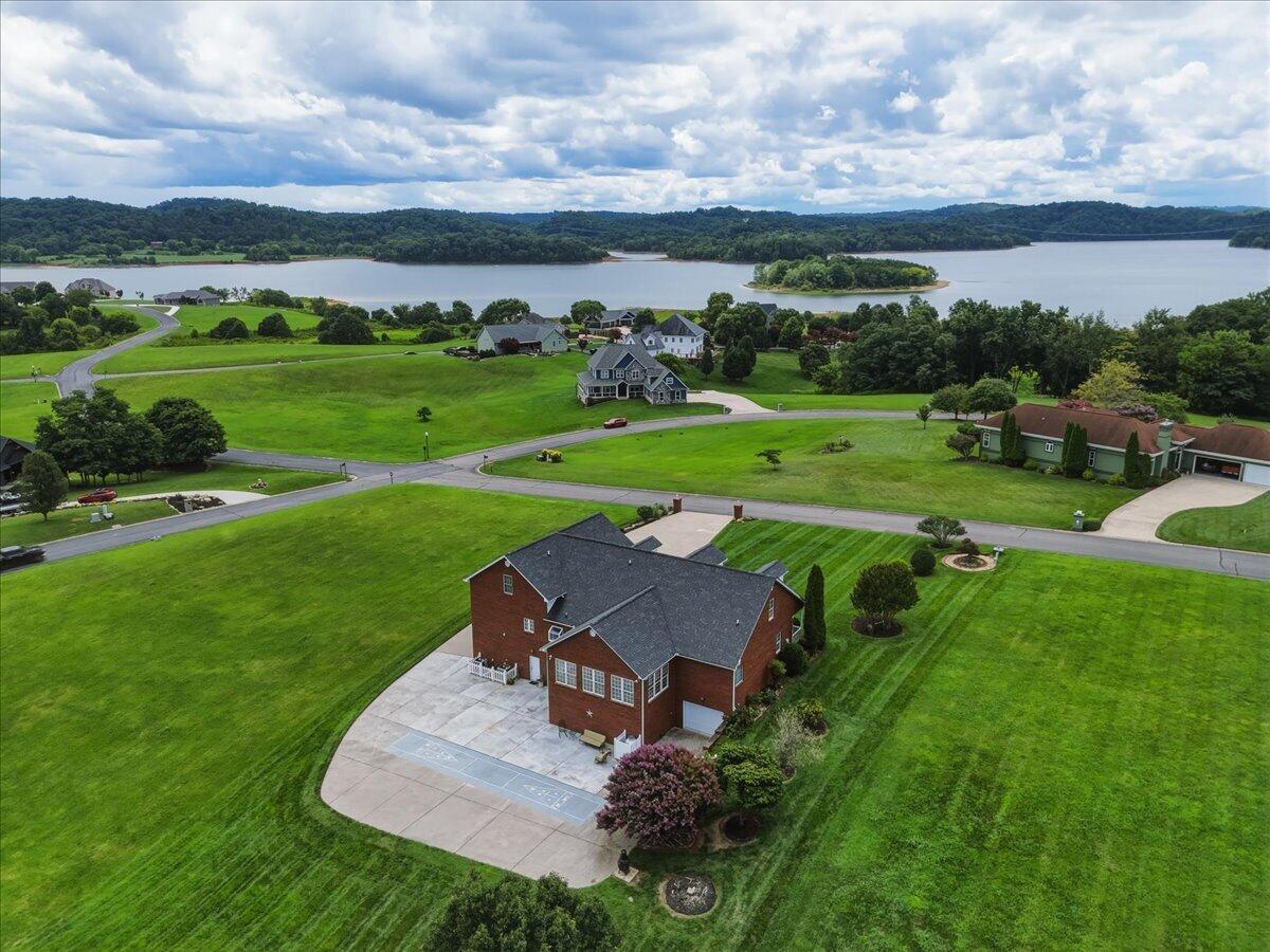 Aerial view of a brick home and broad lawn beside a lake with a wooded island.
