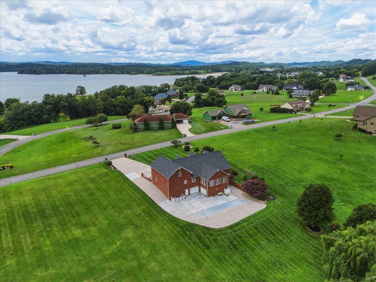 Aerial view of a brick home and broad lawn, with a lake and wooded shoreline beyond.