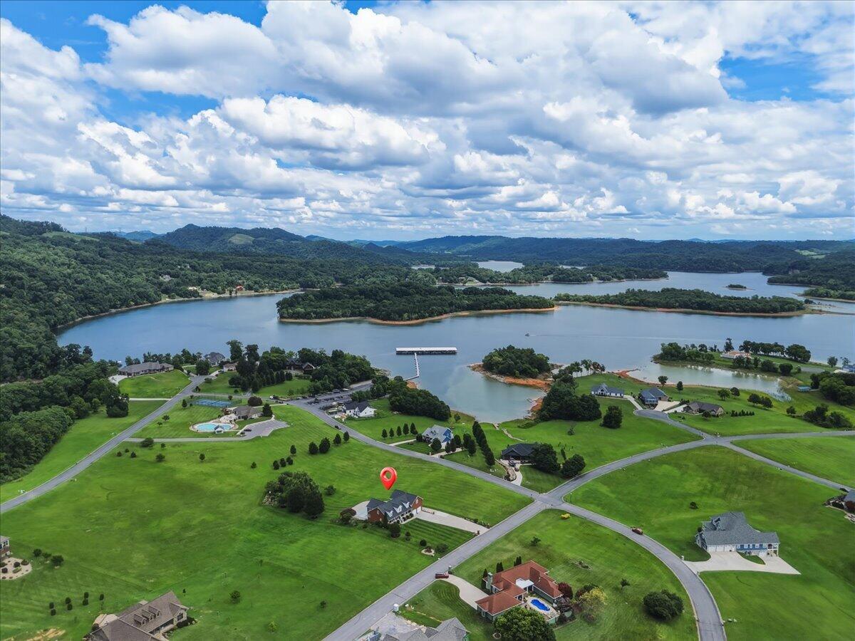 Aerial view of a home beside a lake, with a dock, lawns, and wooded hills.