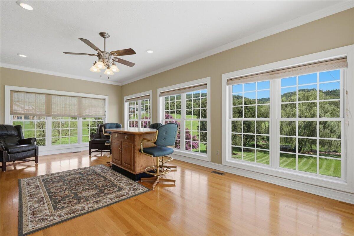 Furnished home office with large windows overlooking a green lawn and wooded hills.