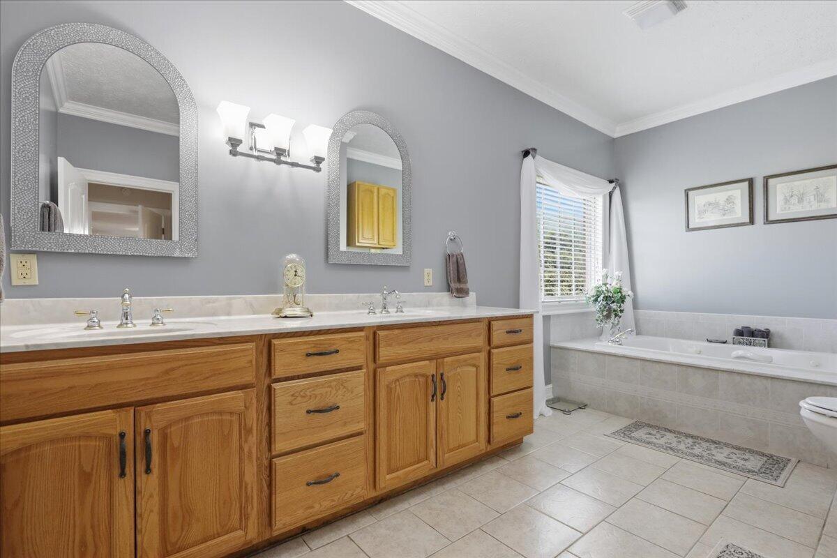 Bathroom with a long oak double vanity and a tiled soaking tub beneath a window.