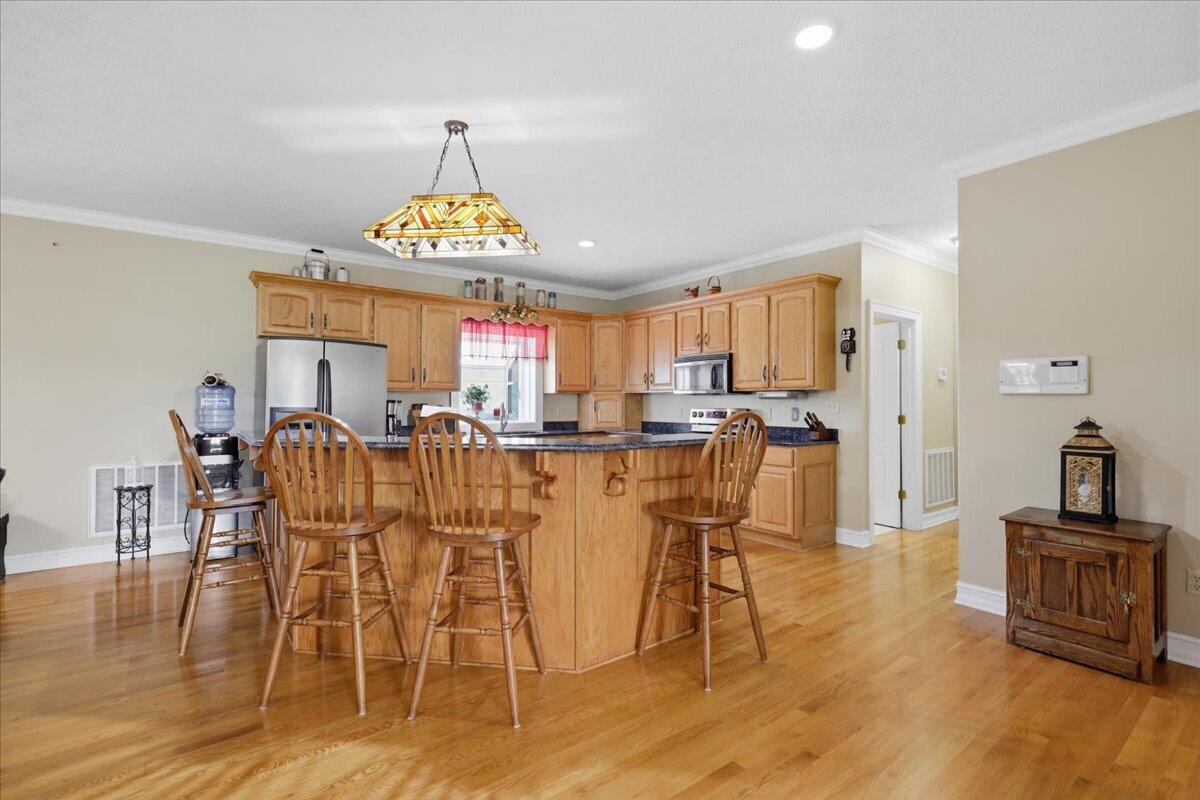 Kitchen with a large wood island, three bar stools, honey-toned cabinets, and hardwood floors.