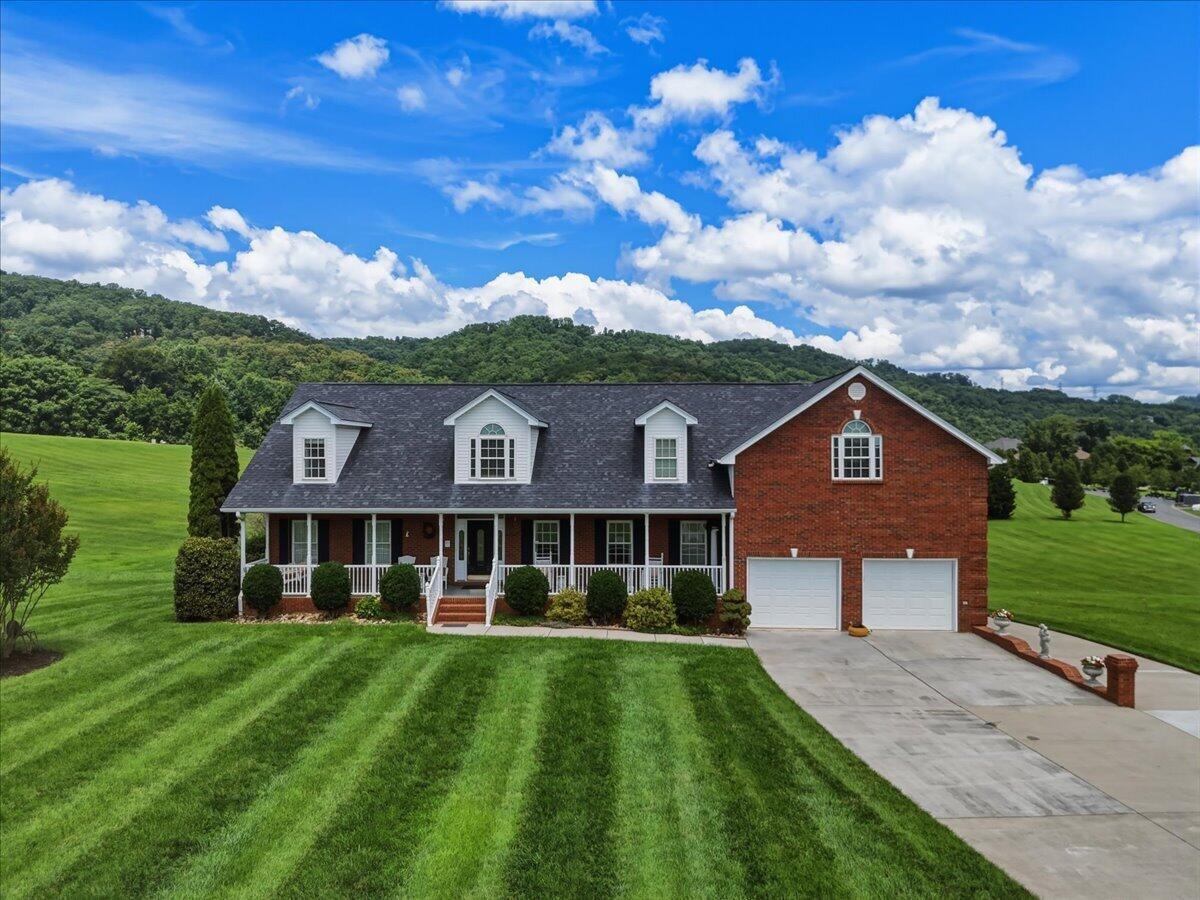Red brick home with a covered porch, dormers, two-car garage, and broad lawn.