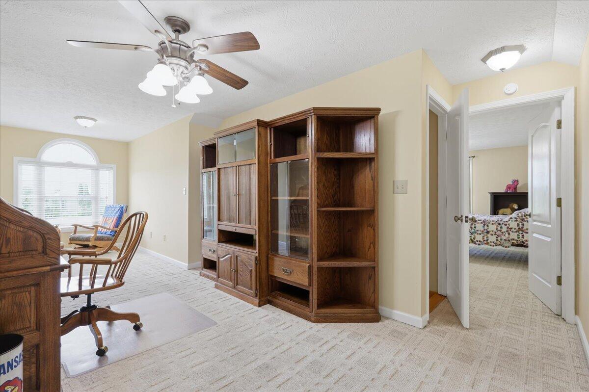Furnished home office with a large wooden cabinet, desk chairs, and an adjoining bedroom visible through the doorway.