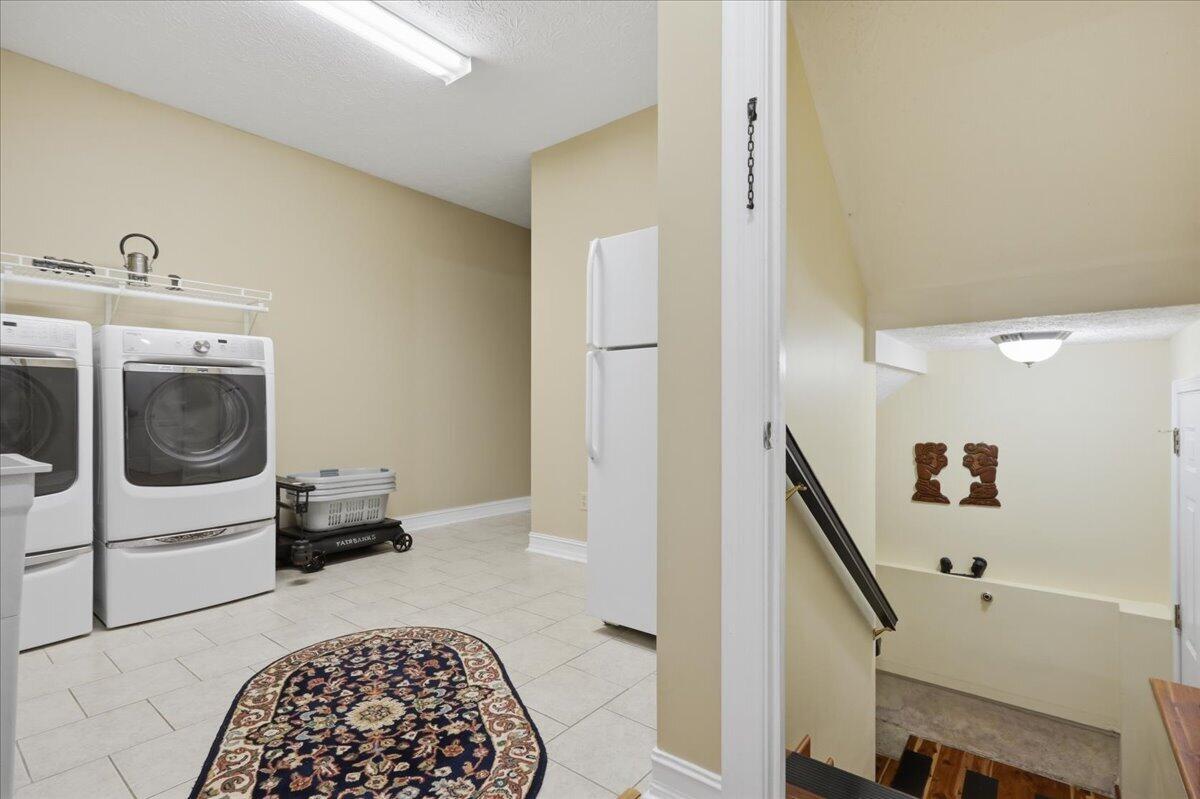 Laundry room with front-loading washers and a refrigerator beside an open stairwell.