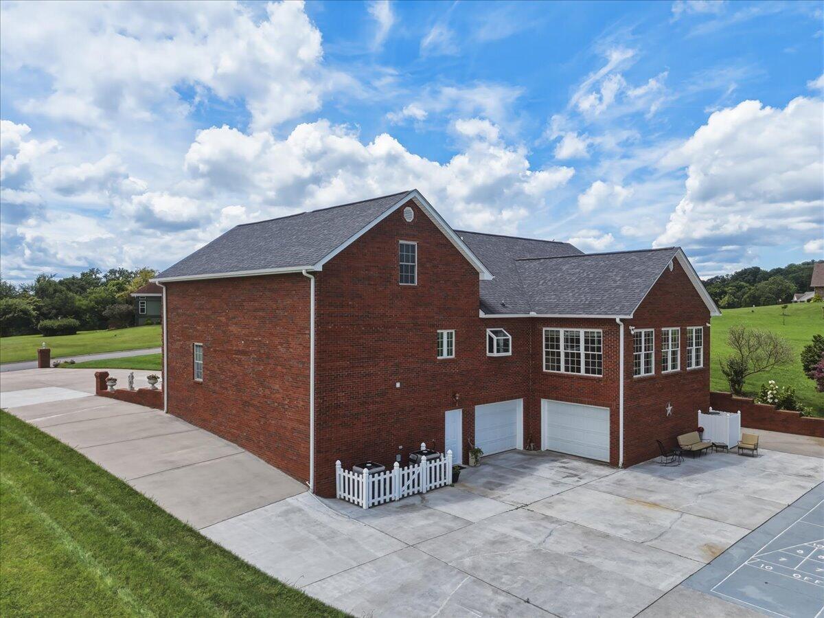 Red-brick home with two garage doors, a broad concrete driveway, and a marked play area.