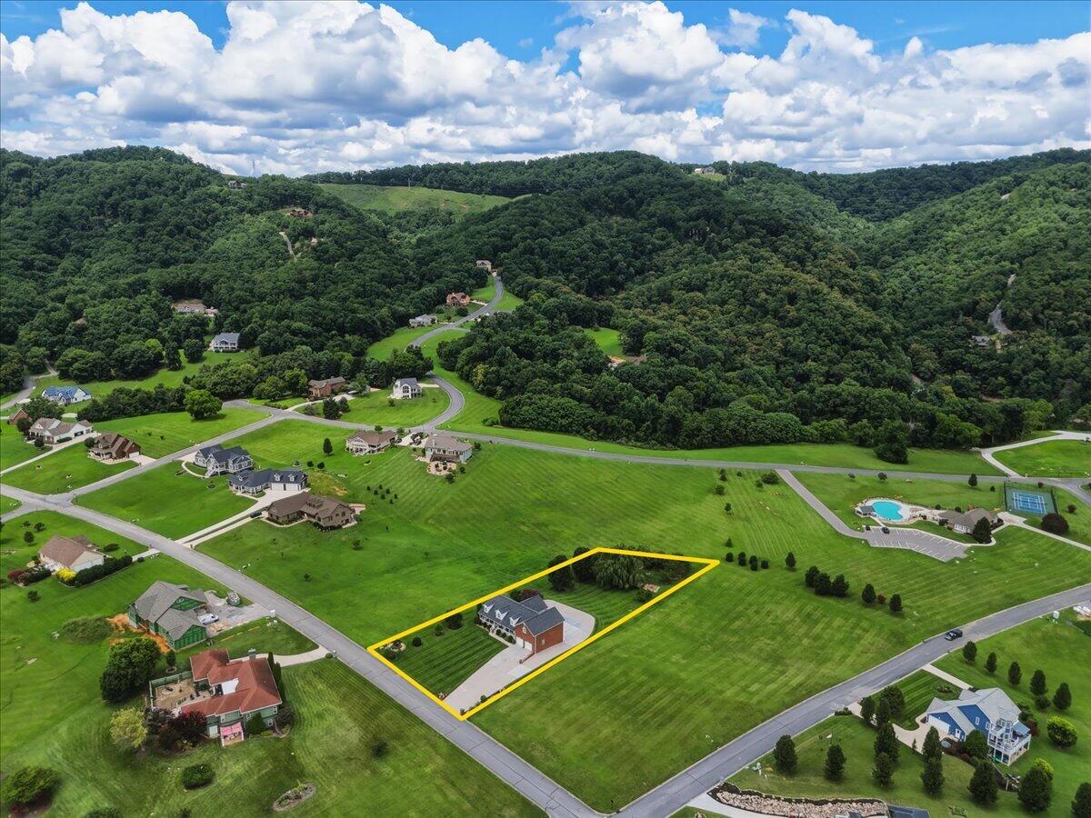 Aerial view of a home on a yellow-outlined lot beside wooded hills.