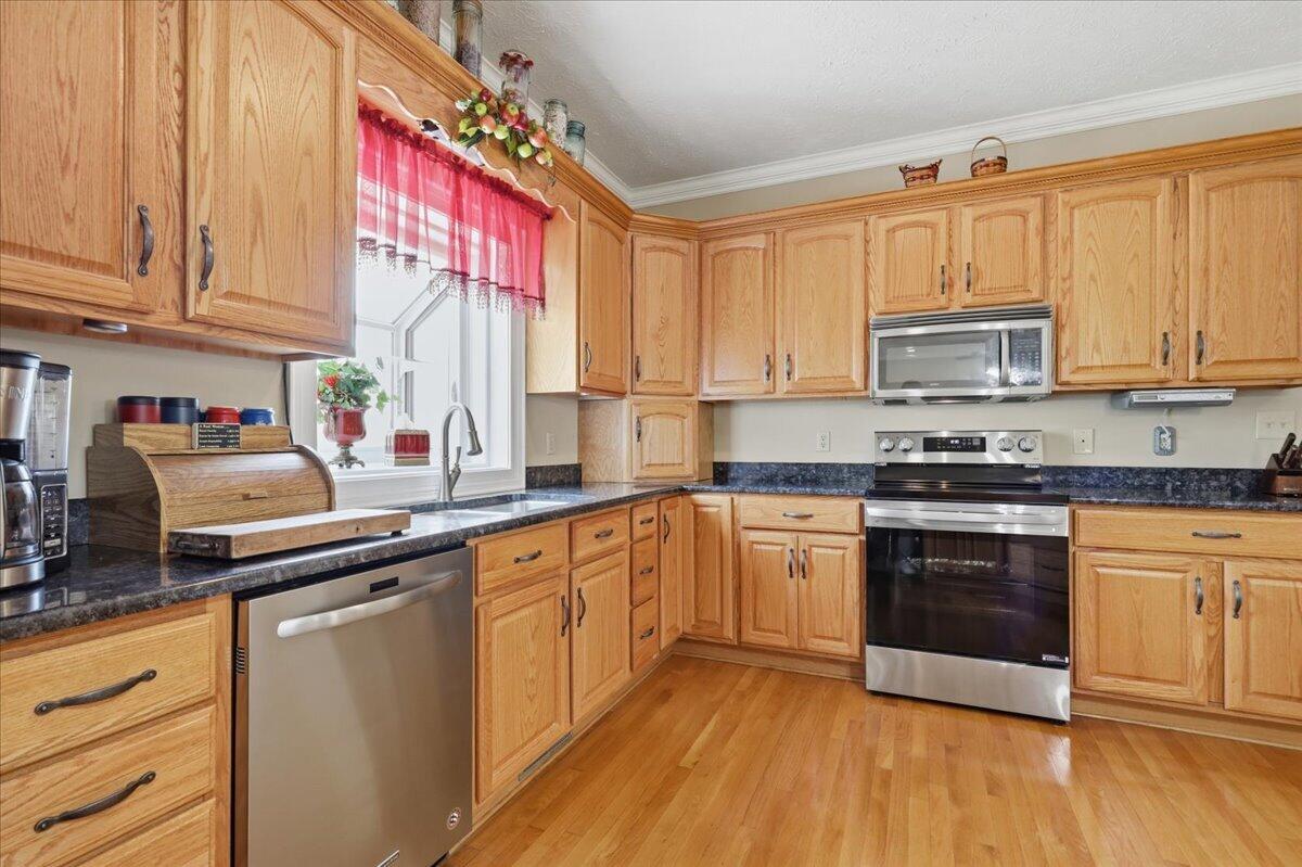 Kitchen with honey-colored cabinets, dark countertops, stainless steel appliances, and a window above the sink.