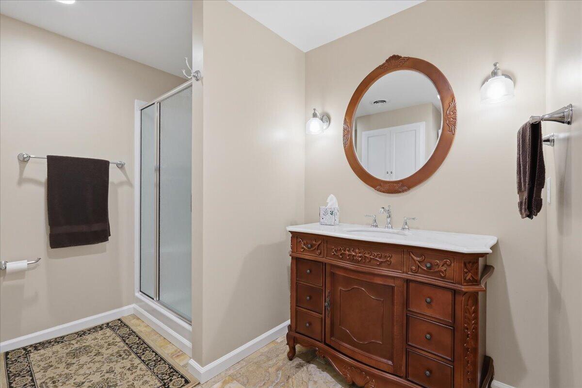 Bathroom with an ornate wood vanity and oval mirror beside a glass shower.