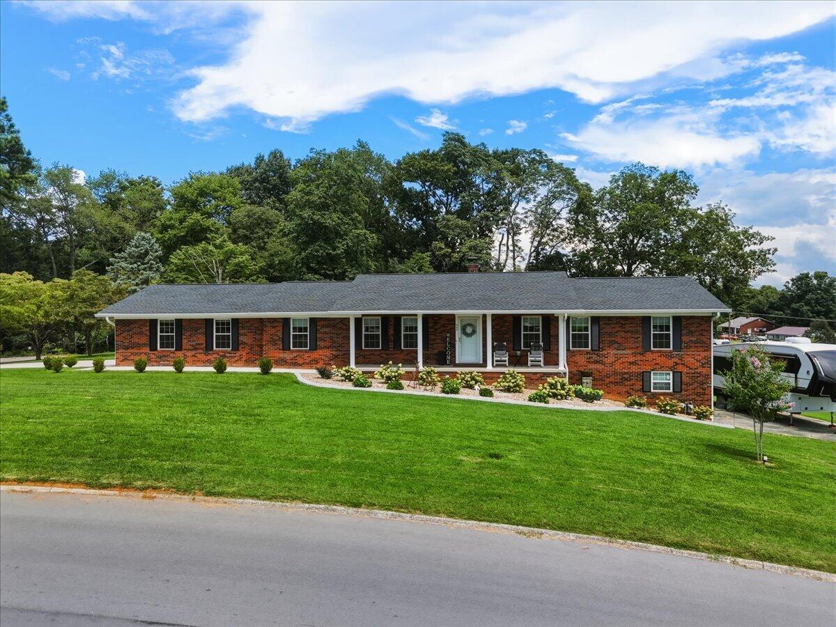 Red brick ranch house with black shutters, a covered porch, and a broad green lawn.