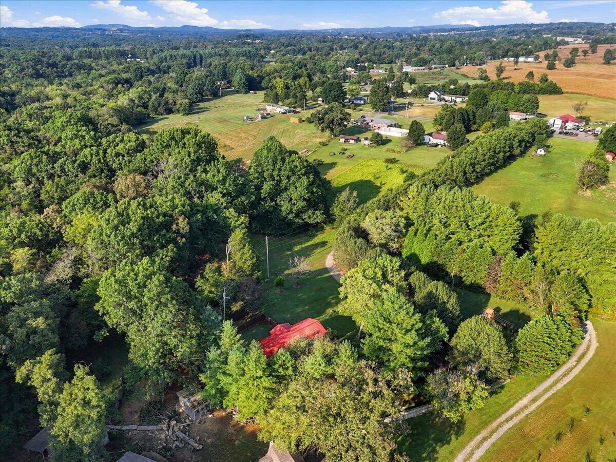 Aerial view of a red-roofed house nestled among trees, with fields and wooded hills beyond.