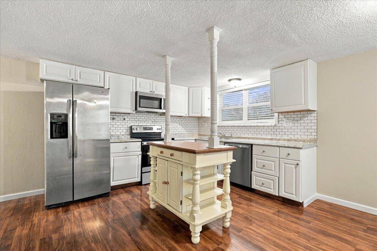 Kitchen with white cabinets, stainless steel appliances, subway tile backsplash, and a cream island with a wood top.