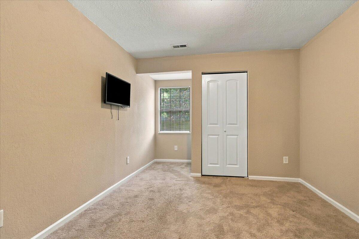 Carpeted bedroom with a wall-mounted TV, window with blinds, and white double-door closet.